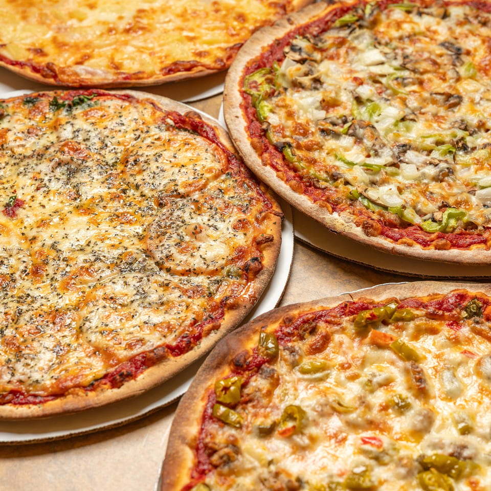 Four delicious pizzas with various toppings, including cheese, vegetables, and herbs, on a table.
