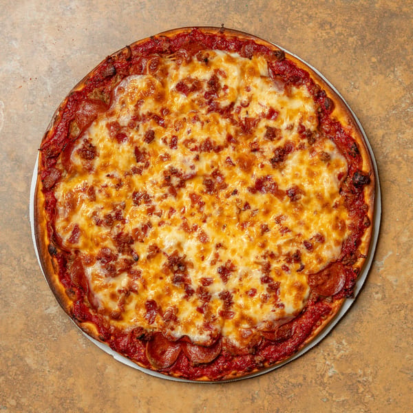 A whole pepperoni and bacon pizza with melted cheese and a thick crust on a brown surface.