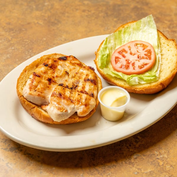 Grilled chicken sandwich on a bun with lettuce, tomato, and a side of mayonnaise.