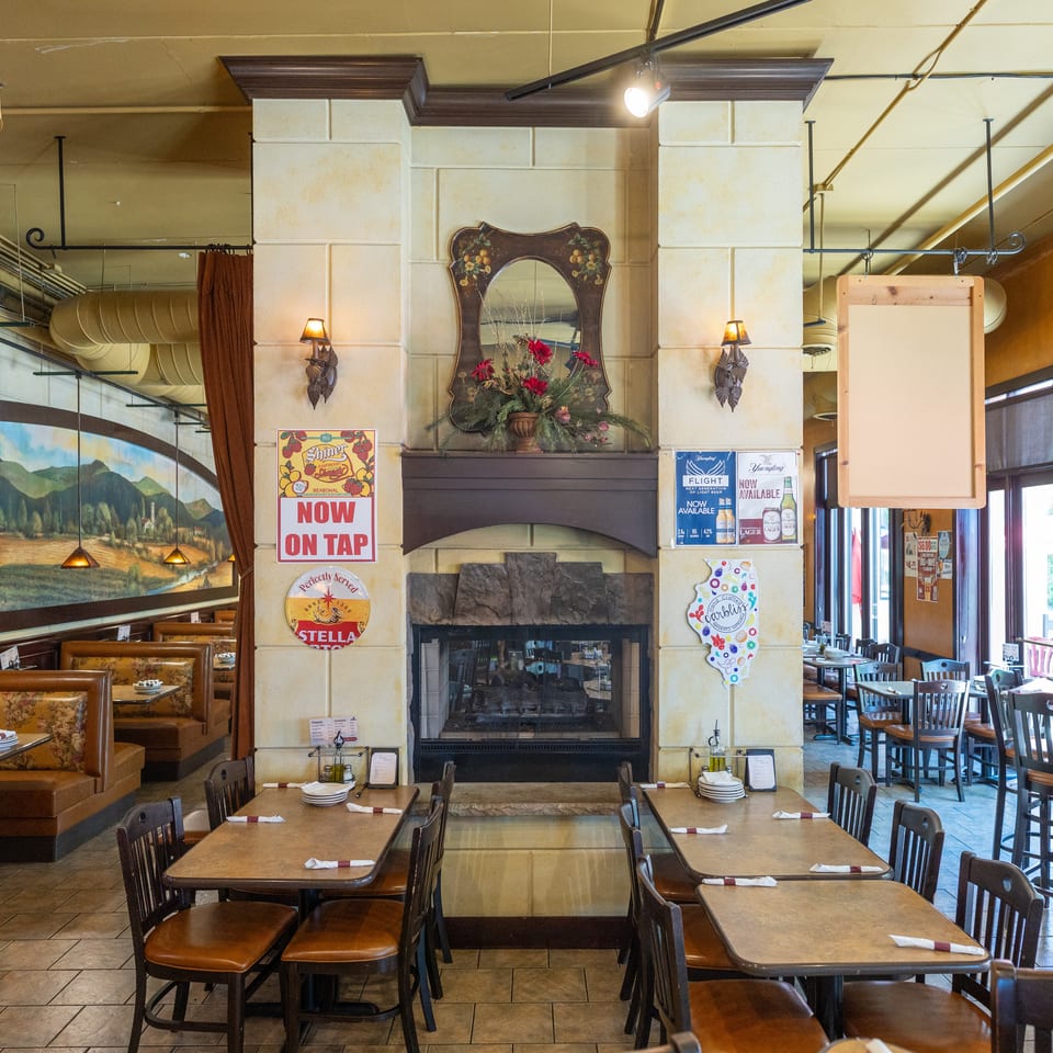 Restaurant interior with a fireplace, booths, tables, chairs, and a large mural on the wall.