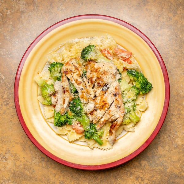 Grilled chicken and broccoli farfalle pasta with parmesan cheese on a yellow plate.