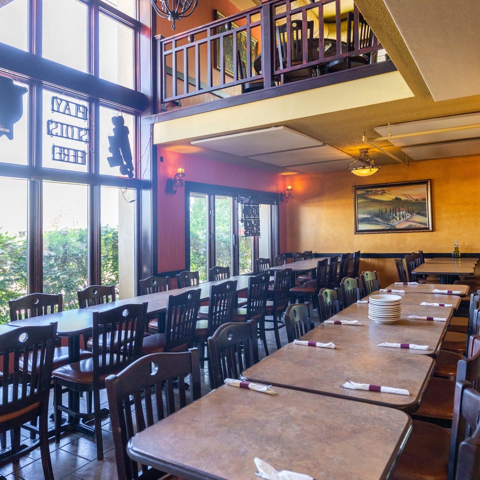 Spacious restaurant dining room with tables, chairs, large windows, and an upper-level seating area.