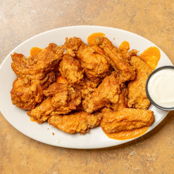 A white oval plate filled with crispy, orange-glazed chicken wings and a side of ranch dressing.