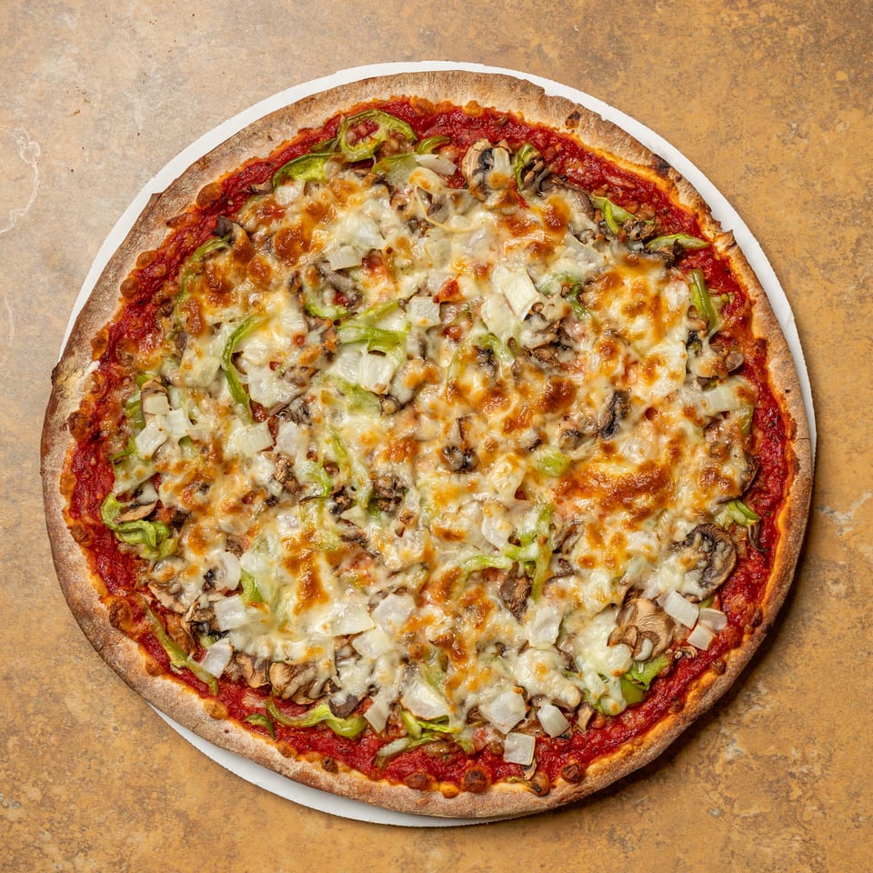 A whole pizza with melted cheese, green peppers, onions, and mushrooms on a white plate.