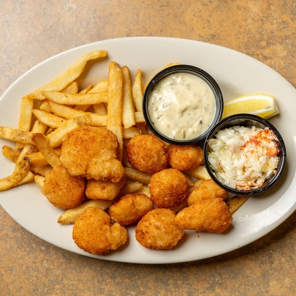 Fried scallops and french fries with tartar sauce, coleslaw, and a lemon wedge.