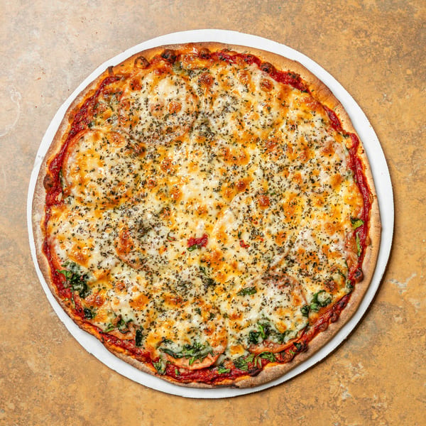 A whole, round pizza with melted cheese, tomato slices, and green herbs on a white plate.