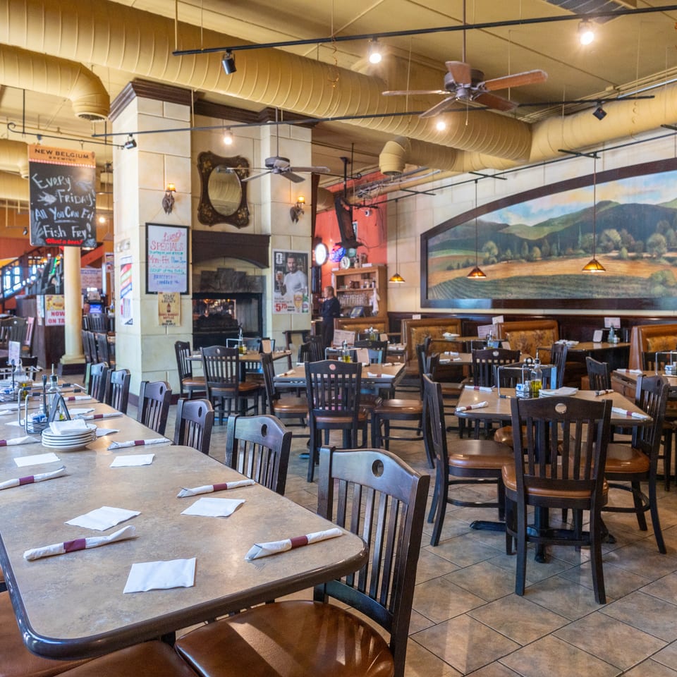 Spacious restaurant interior with multiple dining tables, chairs, and a large landscape mural on the wall.