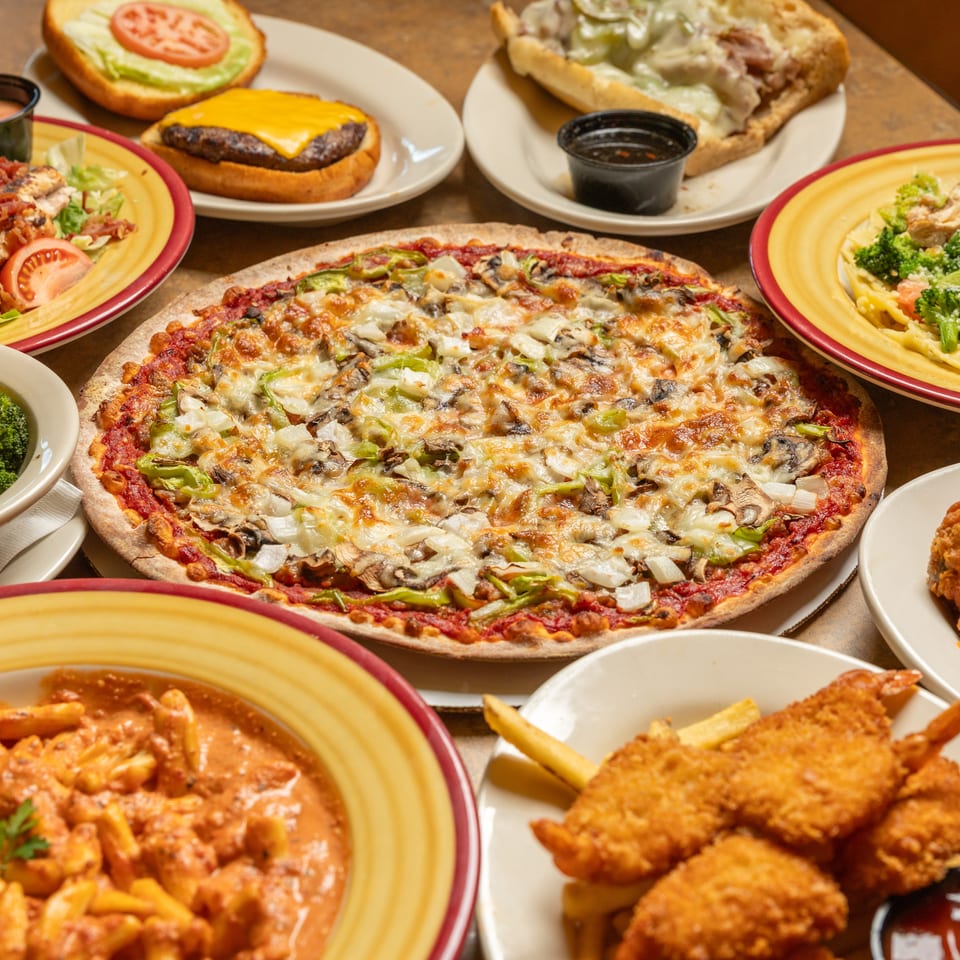A table laden with various dishes including pizza, pasta, burgers, salads, and fried shrimp.