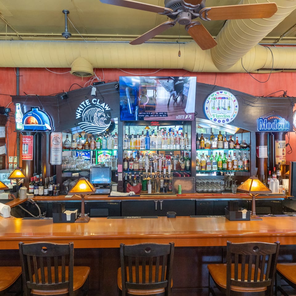 A well-stocked bar with various liquor bottles, beer taps, and bar stools under a ceiling fan.