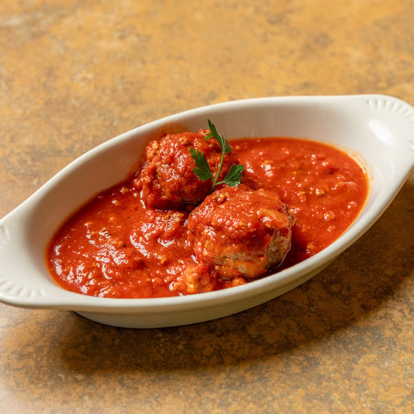 Two meatballs covered in red sauce and garnished with parsley in a white dish.