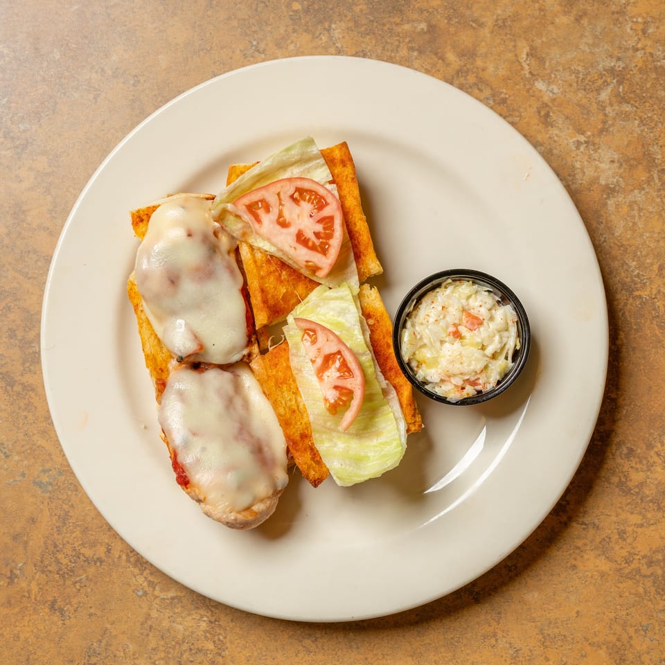 Open-faced sandwiches with melted cheese, lettuce, and tomato, served with a side of coleslaw.