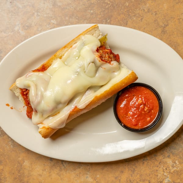 Meatball sub sandwich with melted mozzarella cheese and a side of marinara sauce on a white plate.