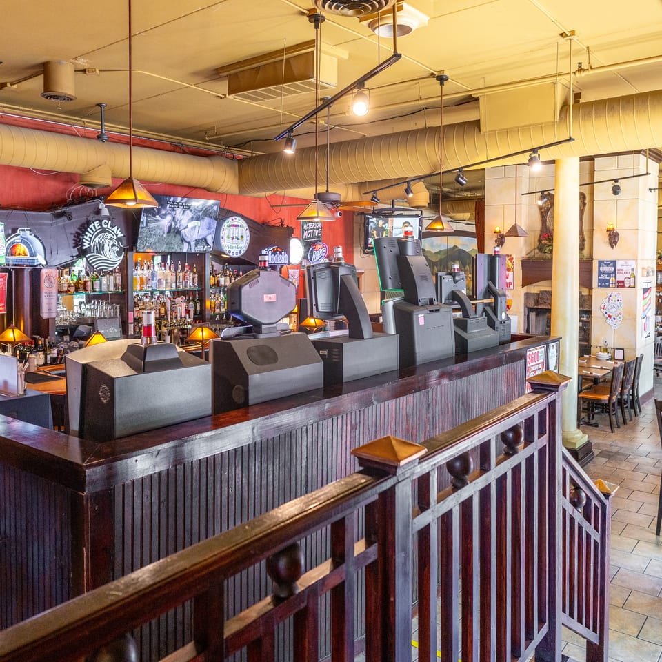 A restaurant interior with a long wooden bar, liquor bottles, TVs, and dining tables.